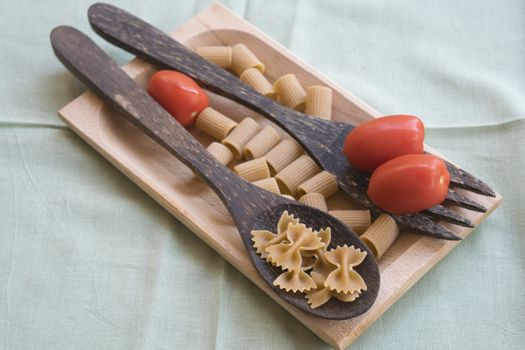 wholemeal butterfly pasta on a wooden ladle and fresh cherry tomatoes