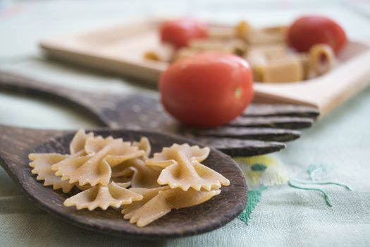 wholemeal butterfly pasta on a wooden ladle and fresh cherry tomatoes