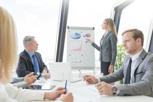 Business presentation of statistics, business woman pointing at flipchart, team of people at meeting table watching