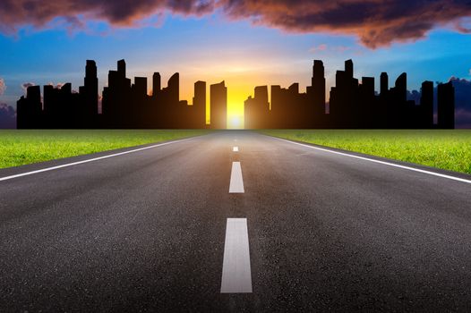 A long straight road and cityscape at sunset.