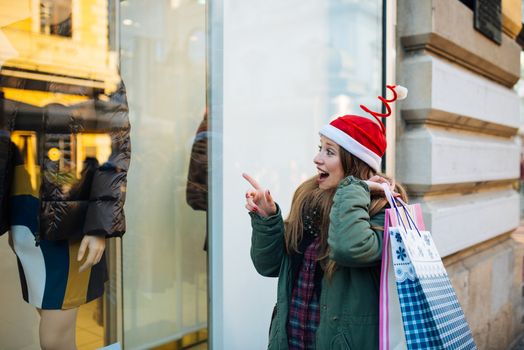 Young attractive woman with santa claus hat in front of shopping window looking to buy something