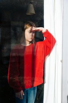 A sad and depressed cute little girl alone near the window. Outdoor portrait of a sad teenage girl.