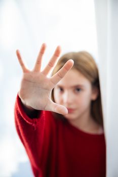 Sad cute little girl suffering depression and standing behind the window during a rainy day with raised hand 