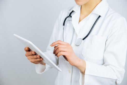 Female doctor with digital tablet. Attractive young female doctor in white lab coat working on digital tablet and standing against white background.