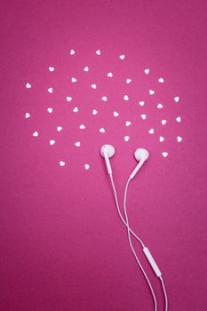 Music love. White earphones surrounded by hearts, on bright magenta background.