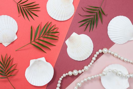 Tropical flat lay with palm leaves, seashells and pearls. Different shades of pink on the background.