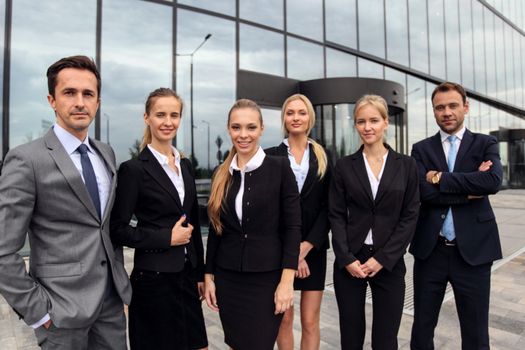 Portrait of successful business people team standing together outdoors near modern office building