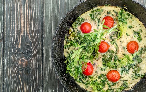 Fritatta in an iron frying pan. Top view of an old wooden table.