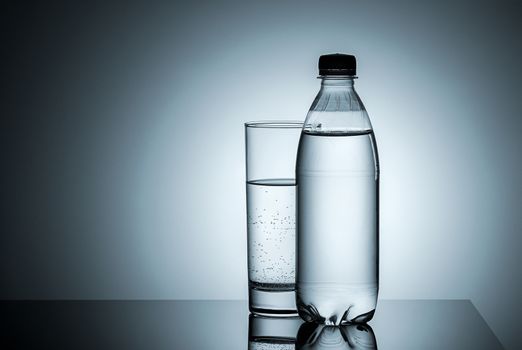 Plastic bottle and glass with water. Gradient background.