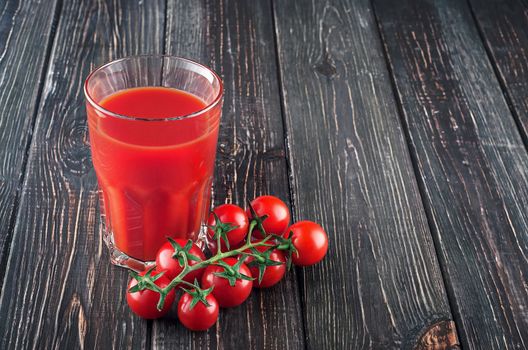 Tomato juice and cherry tomatoes. Glass on a wooden table. Free space.
