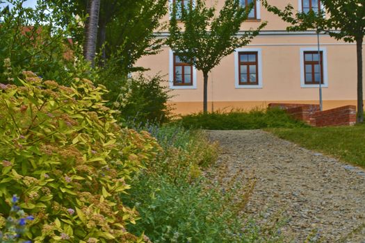 Urban gravel path. Soft colors. Flowers and building on background. Selective focus.