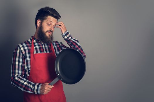 Man in red apron looking at frying pan and thinking