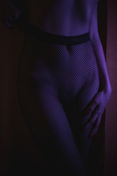 Crop shot of curvy female hips in fishnet tights standing in dark neon lights