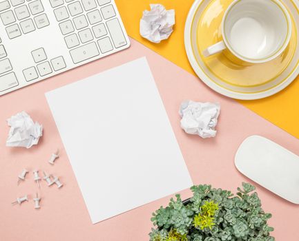 Bright summer home office workspace with blank sheet of paper in the middle. Flat lay composition on pink and yellow background.