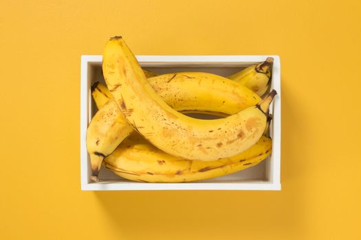 Ripe bananas in a white box on bright yellow background. Summer theme.