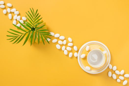 White chocolate candies, palm tree leaves and teacup on yellow background.