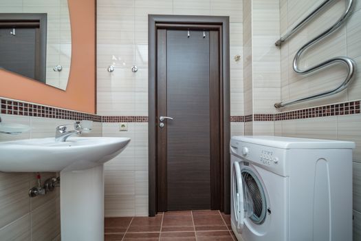 Small beige tile bathroom with bath tube sink and washing machine
