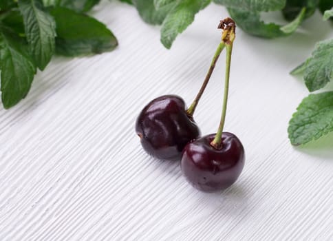 Vinous red cherries with green herbal mix of fresh mint and melissa herbs on white wooden background