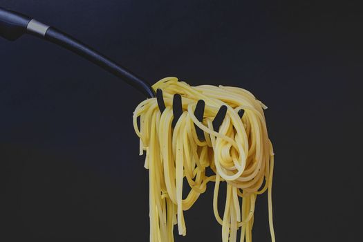 Cooked spaghetti on spaghetti spoon. Spaghetti on black background. Dark food photo. Copy space.