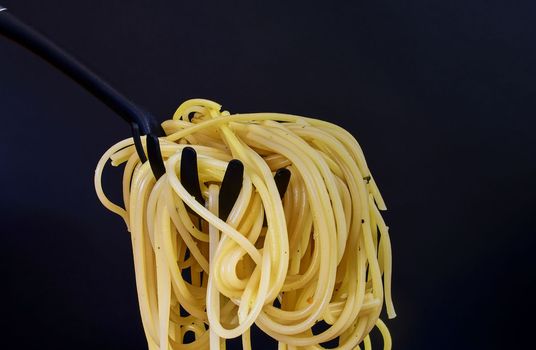 Cooked spaghetti on spaghetti spoon. Spaghetti on black background. Close-up. Dark food photo. Copy space.