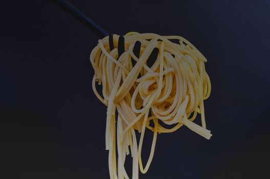 Cooked spaghetti on spaghetti spoon. Spaghetti on black background. Dark food photo. Copy space.