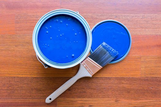 Top view of blue paint can and brush on cherry hardwood floor background