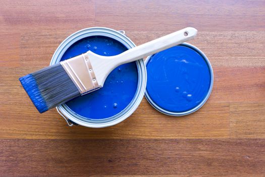 Top view of blue paint can and brush on top with cherry hardwood floor background