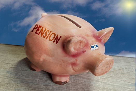 Piggy bank, good luck pig with lettering Pension on wooden surface in front of blue sky background