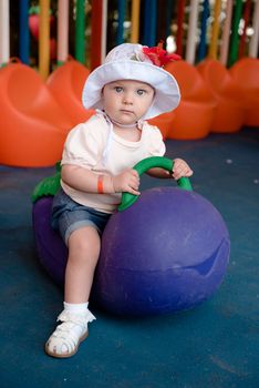 the baby is sitting on a large eggplant and looks at the camera with a serious look, she is on a Playground in a hotel in Turkey. Flower in hat