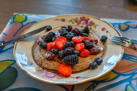 Pancakes made of buckwheat flour with maple syrup and berries of blueberries, blueberries, blackberries and strawberries for breakfast