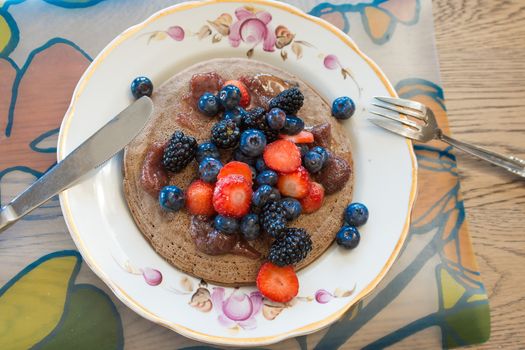 Pancakes made of buckwheat flour with maple syrup and berries of blueberries, blueberries, blackberries and strawberries for breakfast