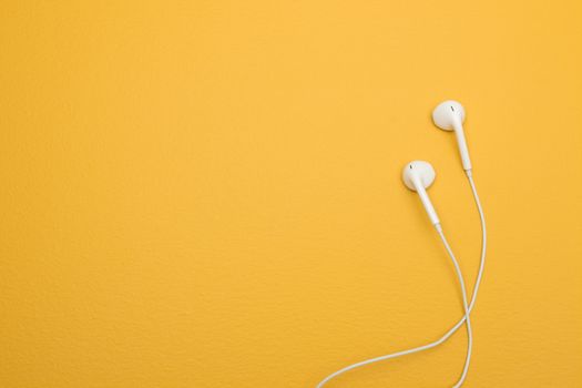 White earphones on yellow background, with copy space on the left.