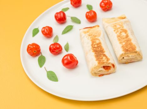 Cooked vegetarian tortillas with tomatoes, cheese and basil, on bright yellow background.
