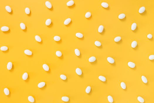 White chocolate candies scattered on joyful bright yellow background.