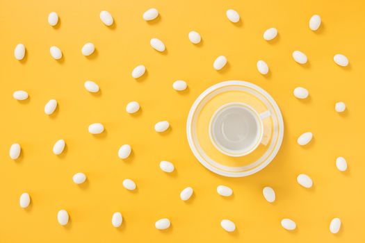 White chocolate candies and teacup on vibrant joyful yellow background.