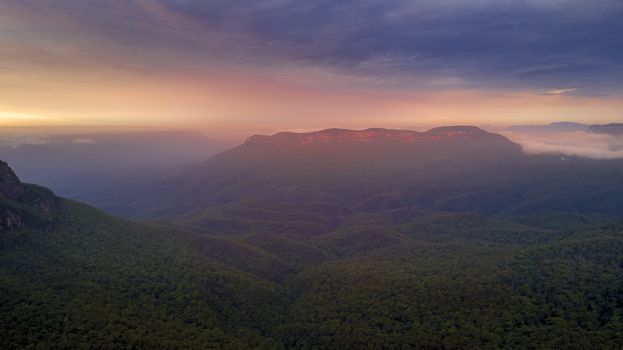 Beautiful sunrise over mist-filled Jamison Valley. In the distance Mt Solitary cliffs catch the warm light. Blue Mountains Australia