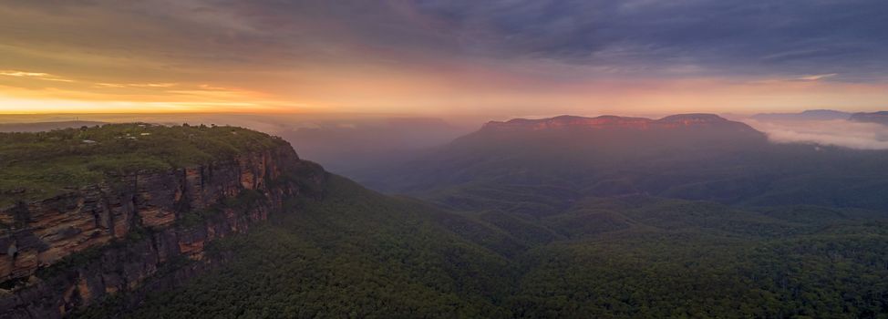 Panorama of the magical sunrise over mist-filled Jamison Valley.  In the distance Mt Solitary cliffs catch the warm light.  Blue Mountains Australia