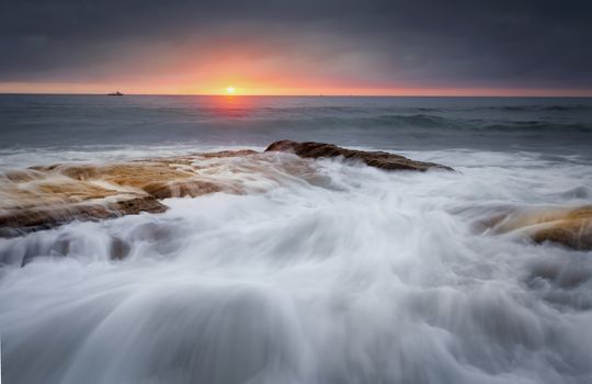 Waves crash over rocks and flow in a myriad of patterns that resemble an artists brush strokes. A break in the storm clouds allowed  a brief viewing of the sun as it rose over the horizon.