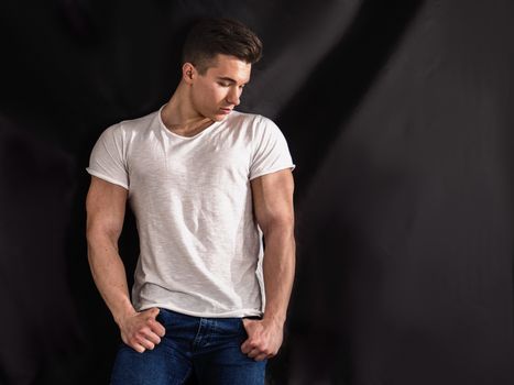 Handsome young muscular man looking down to a side, in studio shot over neutral dark background