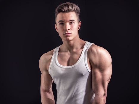 Handsome young muscular man looking at camera, in studio shot over neutral dark background