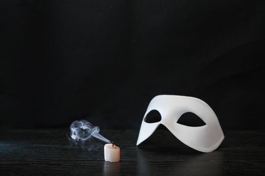 White classical Venetian mask near extinguished candle on dark background