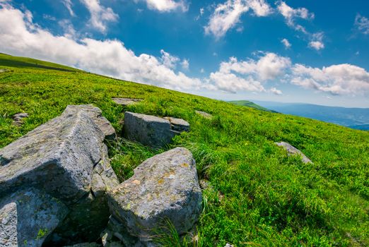 lovely summer landscape. grassy hillside with rocky formations. cloud behind the mountain peak in the distance. bright and fresh day, good mood. wonderful place for hiking and camping