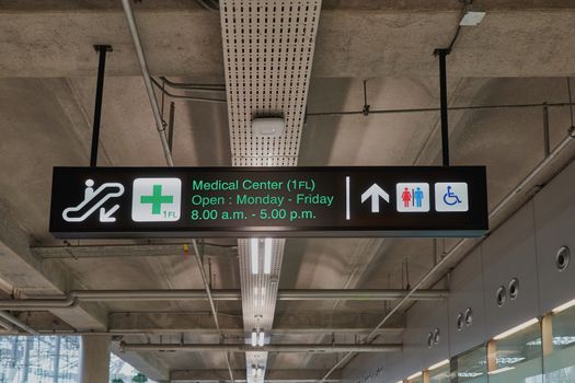 Medical center and toilets information board sign with green character on black background at international airport terminal.