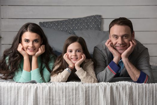 Family portrait of happy parents and their daughter laying on bed at home