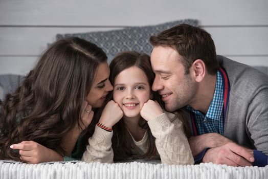 Family portrait of happy parents and their daughter laying on bed at home