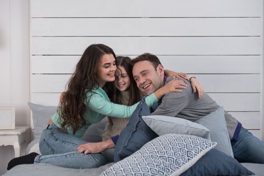 Family portrait of happy parents and their daughter embracing on bed at home