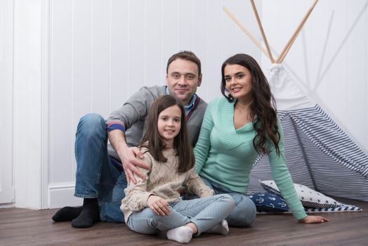 Family portrait of happy parents and their daughter constructed wigwam at home