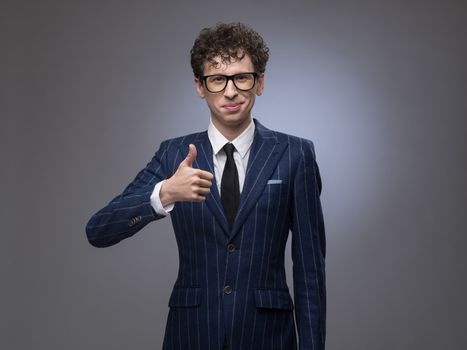 Funny man in striped suit showing thumbs up over gray background. Professional actor facial expression.