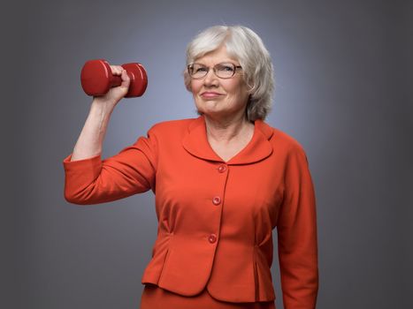 Smiling senior lady with dumbbell on gray background