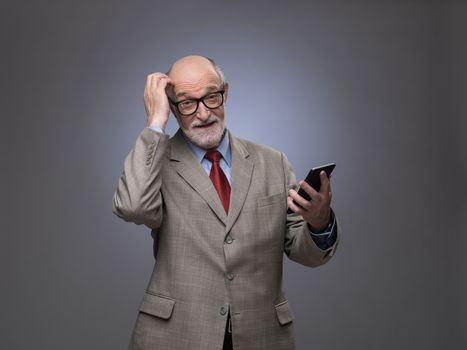 Portrait of funny senior man with phone scratching his head, gray copy space